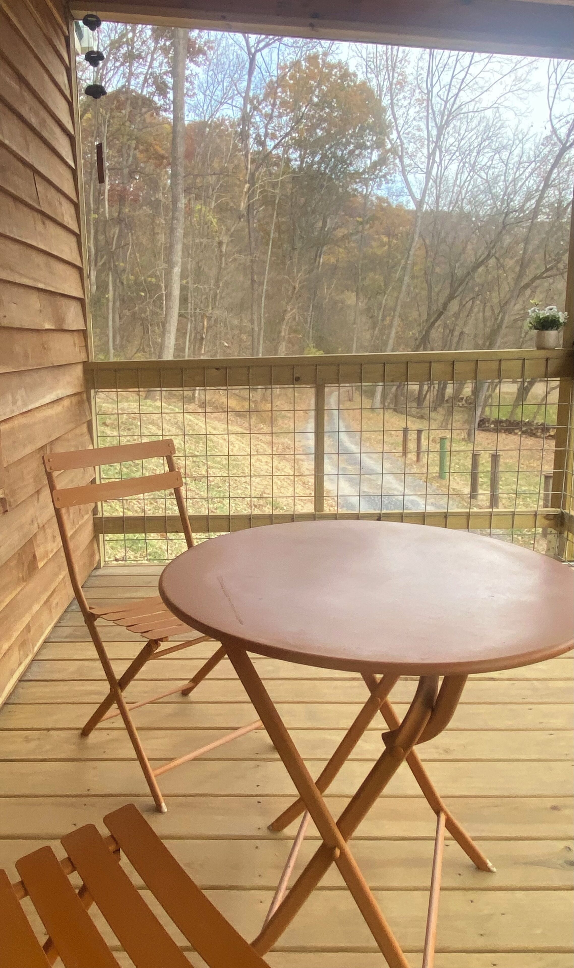 A wooden deck with a round table and two chairs, overlooking a forested area.