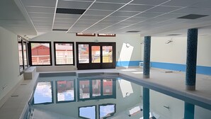 Una piscina interior con paredes de vidrio transparente, suelo de baldosas y techo con diseño de cuadrícula.