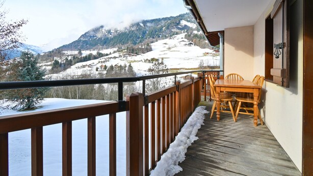 Una terraza de madera con una mesa y sillas, con vistas a un paisaje montañoso nevado.