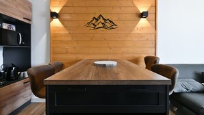 Una mesa de madera para comer con dos sillas, una lámpara fijada a la pared y un panel de madera con un diseño de montaña.