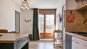 Una cocina moderna con lavavajillas, una mesa de madera y un ventanal corredero que da a un balcón.