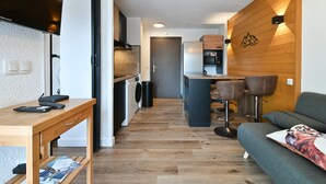 Una cocina compacta con pared de madera, un área de comedor con taburetes y un sofá con cojín.