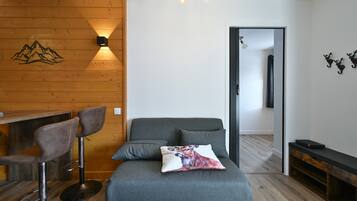 Une pièce avec un mur en bois, un canapé, deux tabourets de bar, un coussin orné d’un motif de renard et un banc.