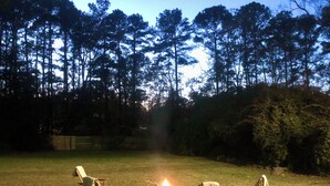 Un patio trasero con un pozo de fuego, tres sillas de madera y una mesa de madera.