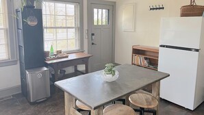 Una cocina compacta con refrigerador, un lavamanos pequeño, una ventana con persianas, una mesa de madera y una planta en maceta.