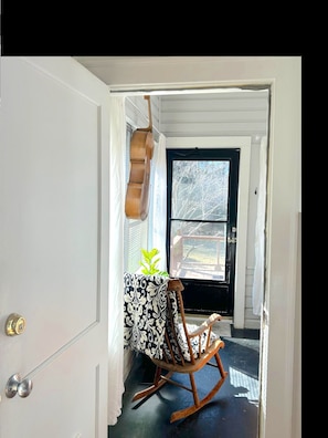 A room with a wooden rocking chair, a small table with a patterned tablecloth, and a window with a view of trees.