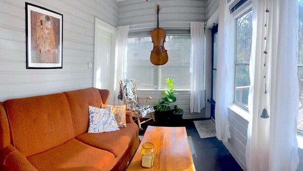 Una habitación acogedora con un sofá, un violín colgado, un cuadro enmarcado y vistas a una terraza.