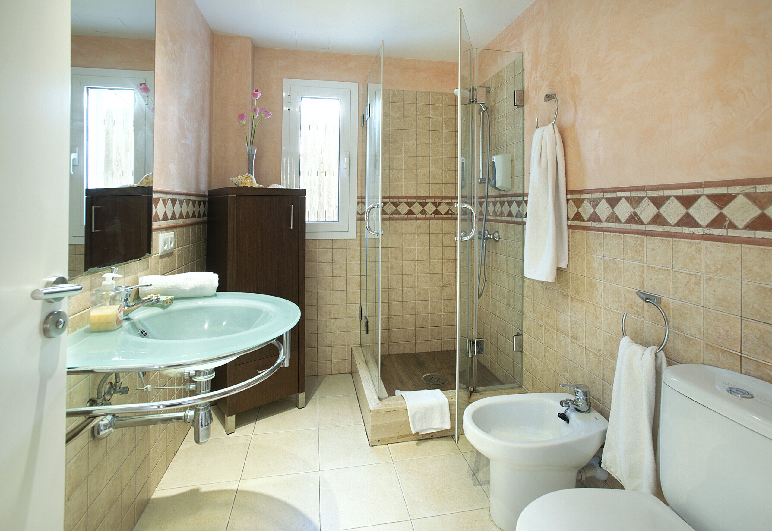 A bathroom with a glass-enclosed shower, a sink, a bidet, and a toilet.