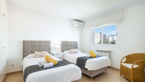 Una habitación de hotel con dos camas, una ventana con vistas, una silla de mimbre y un equipo de aire acondicionado.