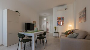 A modern living room with a sofa, a dining table with chairs, a television, and artwork on the walls. - Tripoli White Home by Wonderful Italy (Torino)