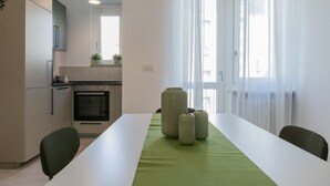 A modern kitchen with white cabinets, a built-in oven, and a dining area with a white table and green runner. - Tripoli White Home by Wonderful Italy (Torino)