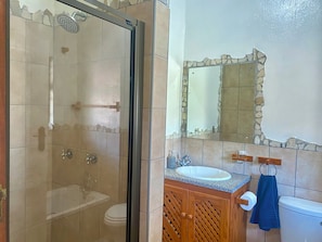 A bathroom with a glass-enclosed shower, a sink with a granite countertop, wooden cabinets, a toilet, and a mirror with a stone frame. - Crayfish Inn no.7 (Ramsgate)