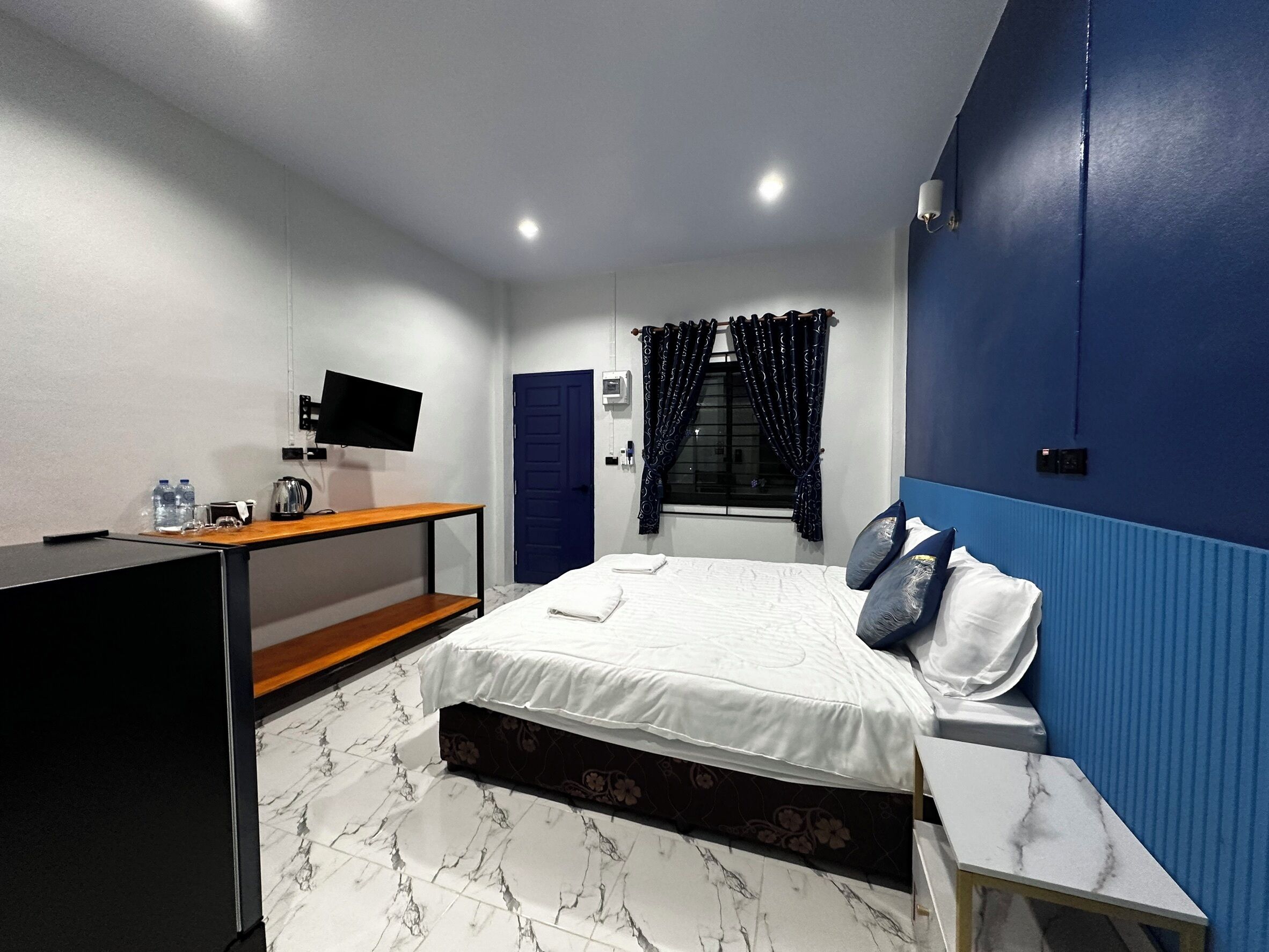 A bedroom with a bed, bedside table, desk, and a TV mounted on the wall.