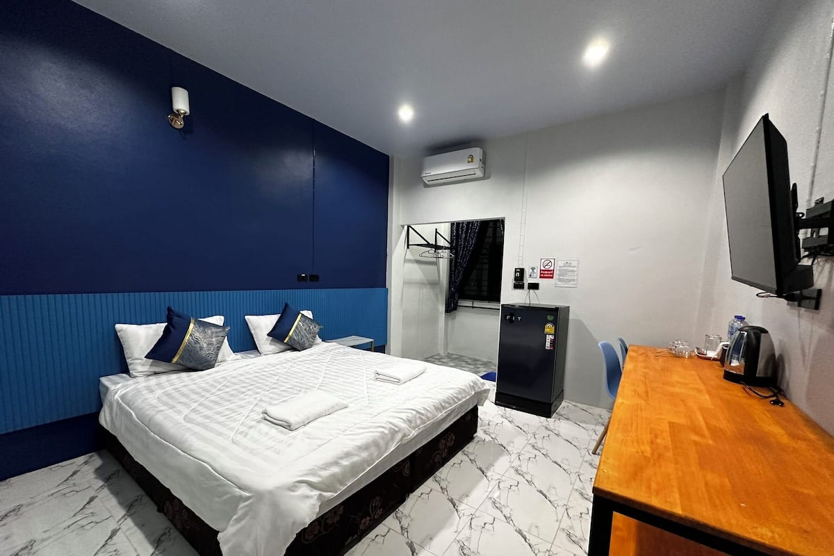 Quarto de hotel com cama, escrivaninha, espelho, ar condicionado e janela com cortinas.