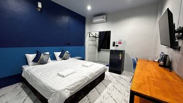 A hotel room with a bed, a desk, a mirror, an air conditioning unit, and a window with curtains.