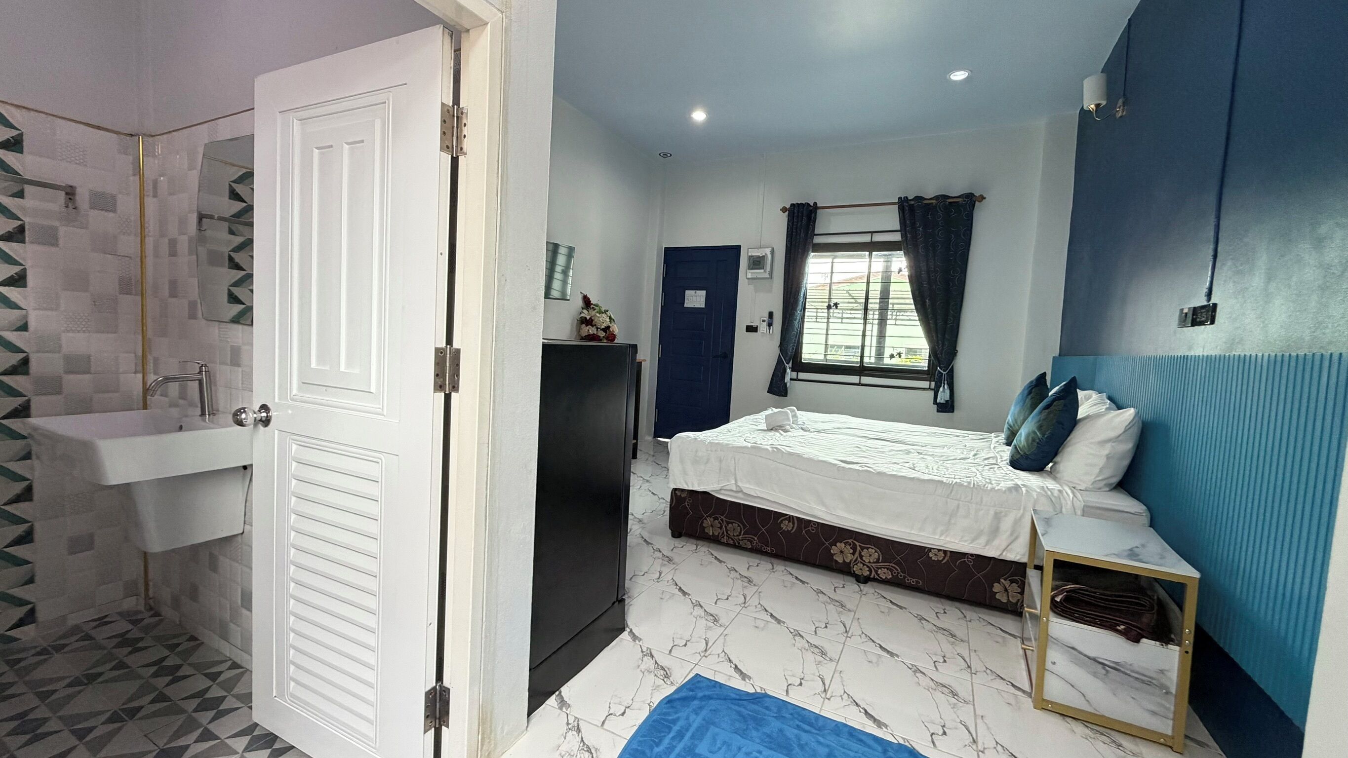 Un dormitorio con cama, cómoda, ventana con cortinas, lavamanos y zona de ducha.