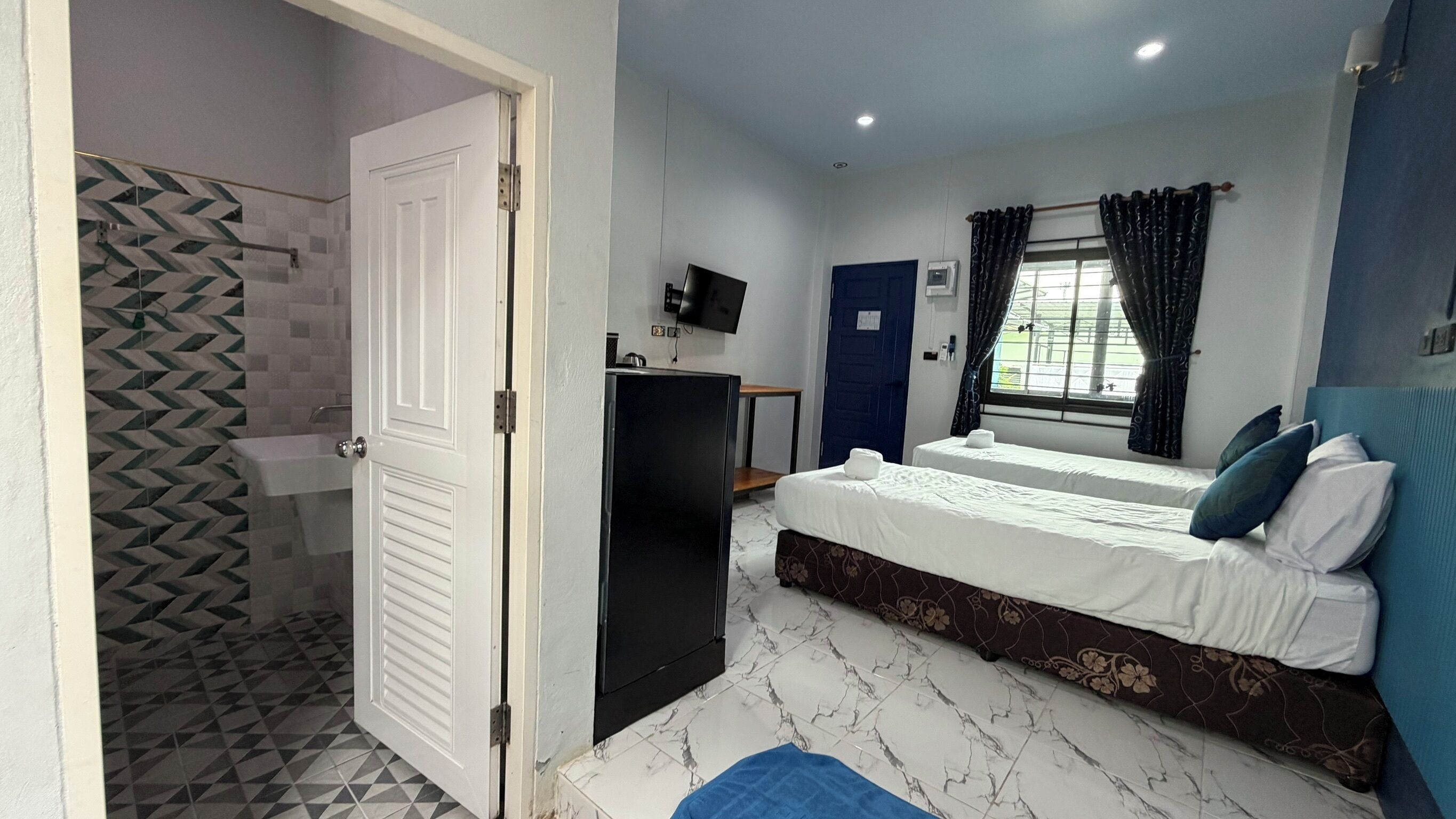 A hotel room with a bed, a desk, a TV, and a shower area.