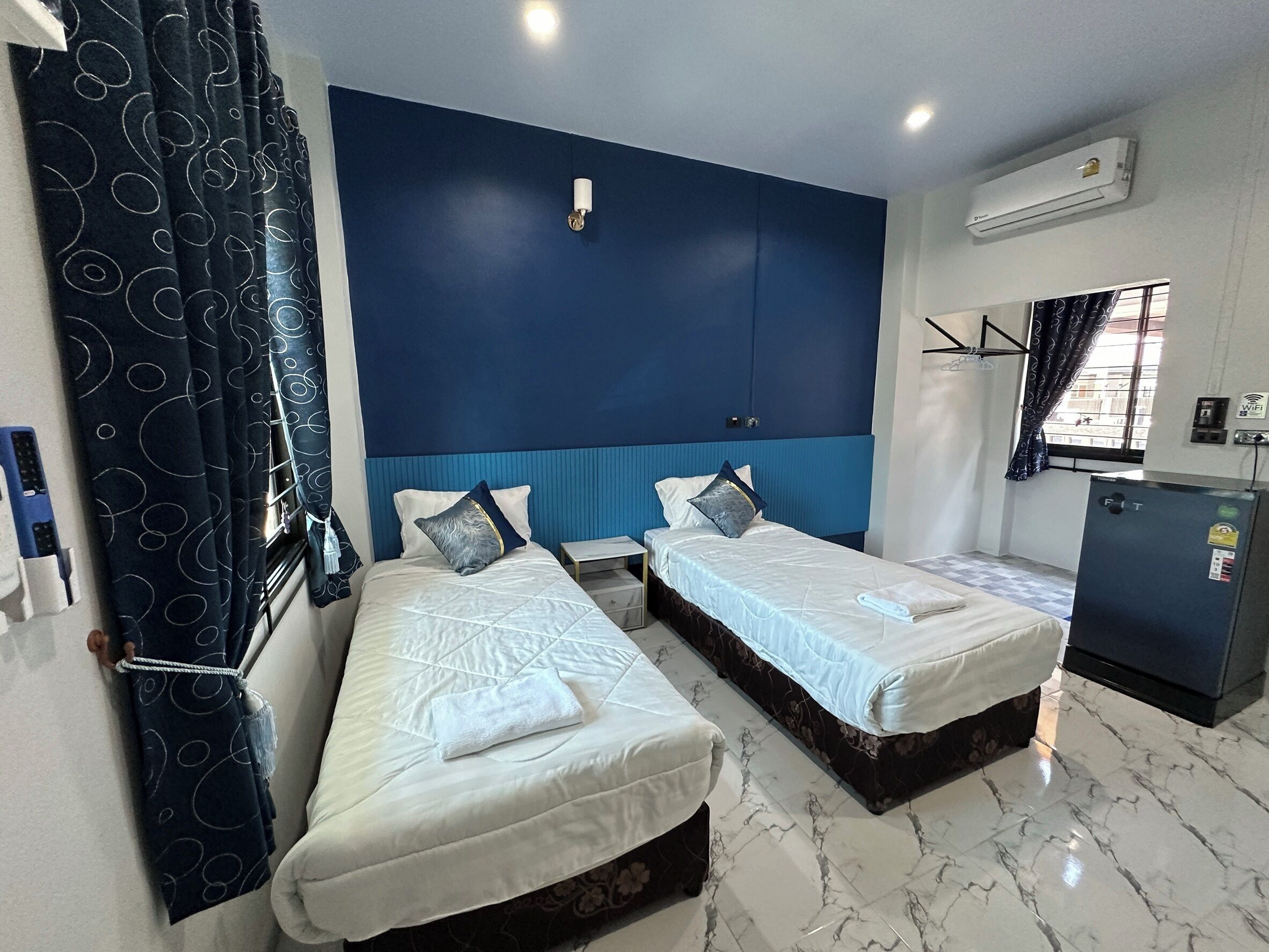 Habitación de hotel con dos camas individuales, una mesita, un armario, un equipo de aire acondicionado y una ventana con cortinas.