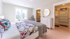 A bedroom with a bed, bedside table, dresser, and a walk-in closet.