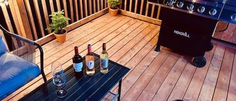 A wooden deck with a grill, potted plants, and a table with bottles and glasses.