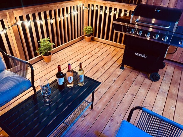 En träaltan med en grill, krukväxter och ett bord med flaskor och glas.