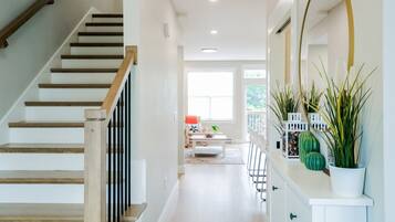 Un intérieur moderne avec un escalier en bois, un coin repas avec une table et des chaises blanches, et un meuble blanc agrémenté de plantes décoratives.