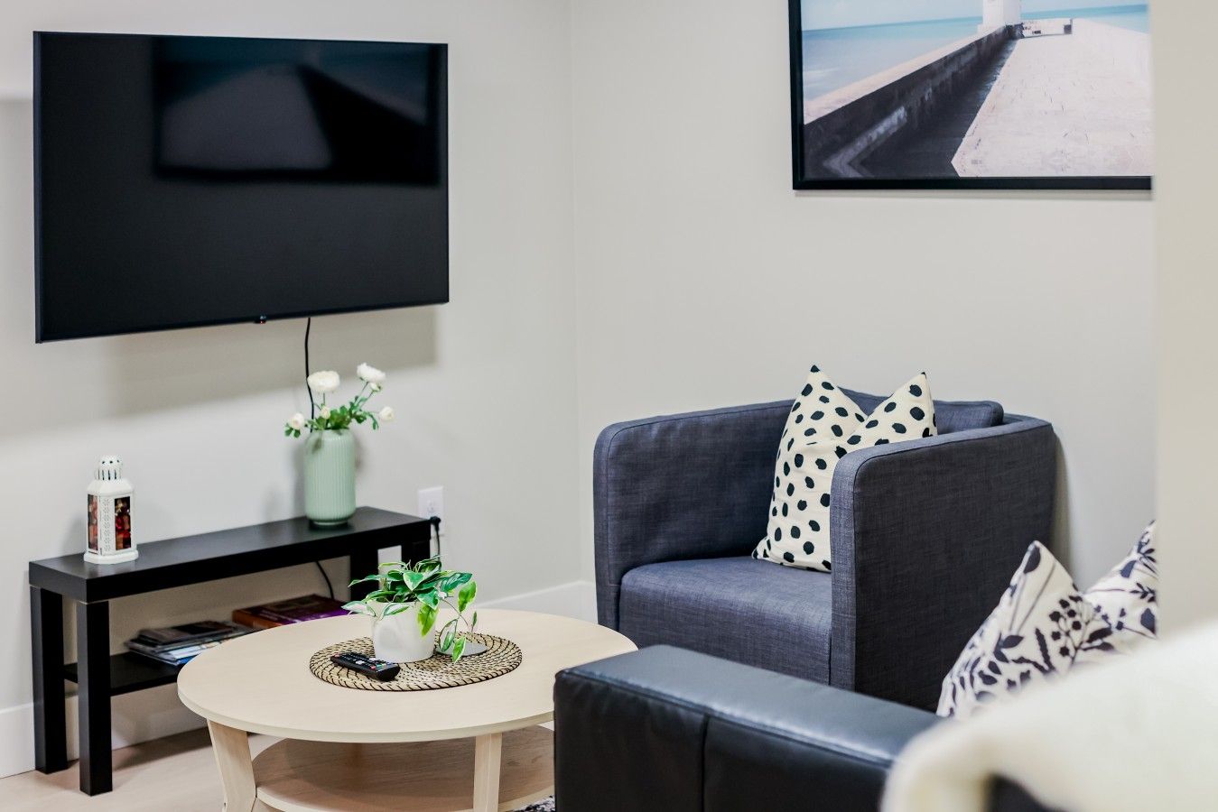 Un salón con televisor de pantalla plana montado en la pared, un sofá con cojines estampados, una mesa de centro con una planta y una mesita auxiliar con adornos.