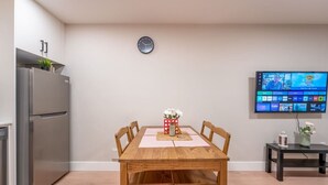 Una cocina moderna con una mesa de comedor de madera, sillas, un refrigerador empotrado, un reloj y un televisor de pantalla plana mostrando un canal deportivo.