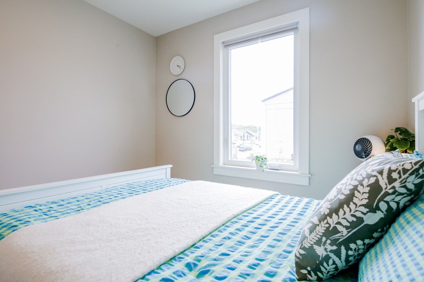 A bedroom with a bed, a window, a wall clock, and a small plant.