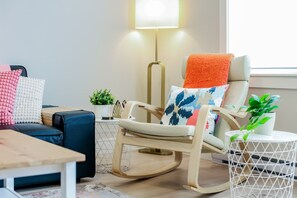 Una sala de estar moderna con una mecedora, un sofá, una mesita y una lámpara.