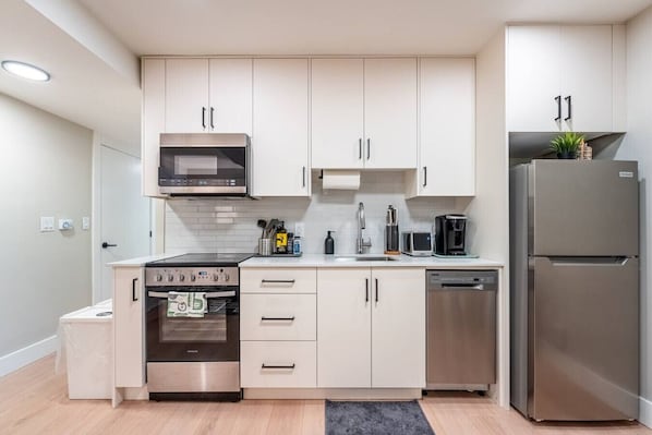 A modern kitchen with white cabinets, stainless steel appliances, and a built-in oven. - New Lux 2BR Bright & Spacious Walk-Out Suite in Halifax (Halifax)