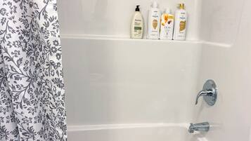 Een badkamer met een wit bad, een douche en een plank met toiletartikelen.