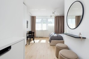 Una camera d'albergo moderna con un letto, una scrivania, una sedia, uno specchio grande e un poggiapiedi.