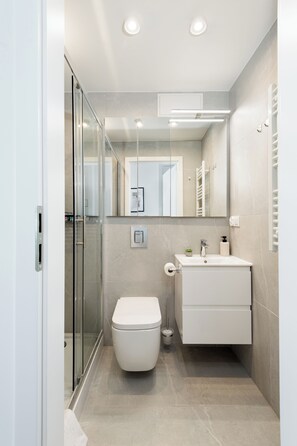 Un bagno moderno con box doccia in vetro, un water bianco, un mobile lavabo con specchio e un porta asciugamani.