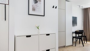Una habitación moderna con un armario blanco, un cuadro enmarcado, un pequeño jarrón con flores y un área de comedor con mesa y sillas.