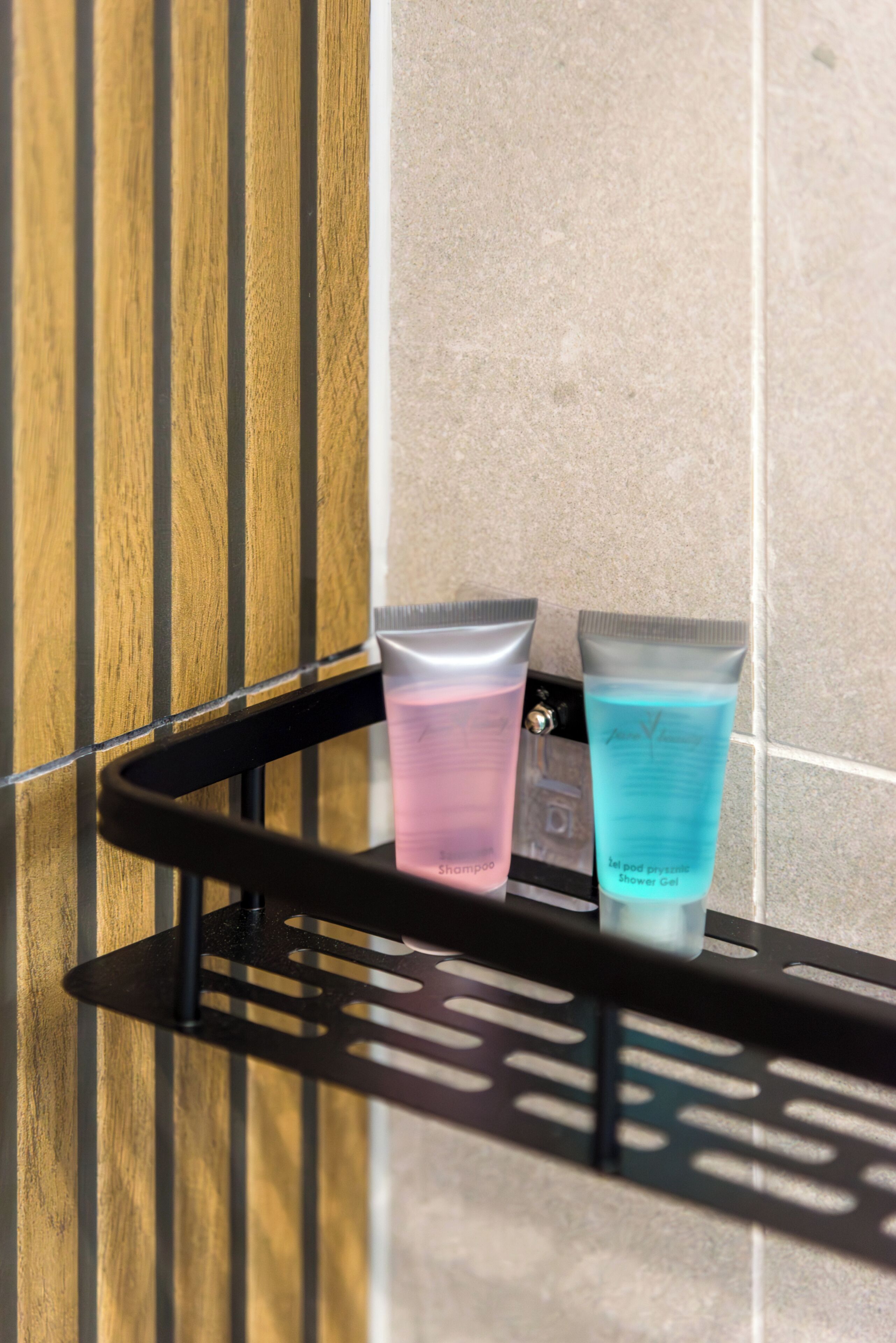 Une salle de bain avec une étagère en métal noir sur laquelle reposent deux récipients contenant des articles de toilette, l’un rose et l’autre bleu, le tout adossé à un mur carrelé.