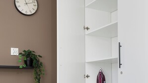 Un dormitorio con cama, lavadora, reloj y estante con una planta.