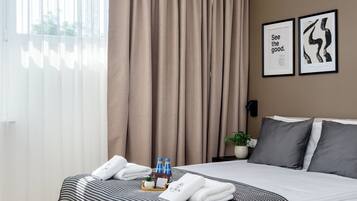 A modern hotel room with a large bed, a ceiling fan, a bedside table with a plant, and a view of the outdoors.