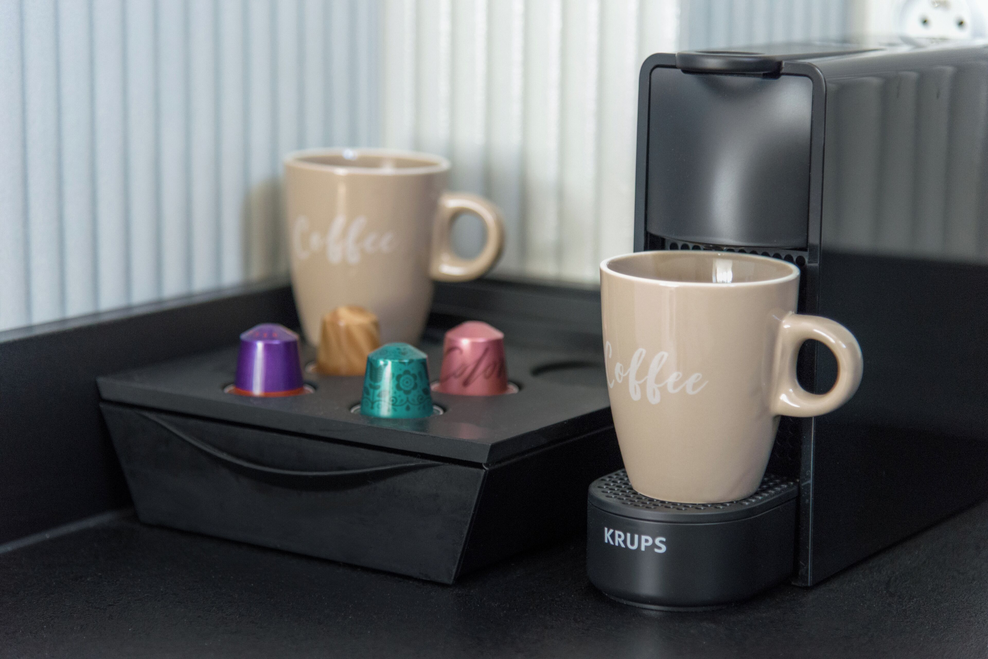 To kaffekopper på en sort bakke med en Krups kaffemaskine ved siden af.