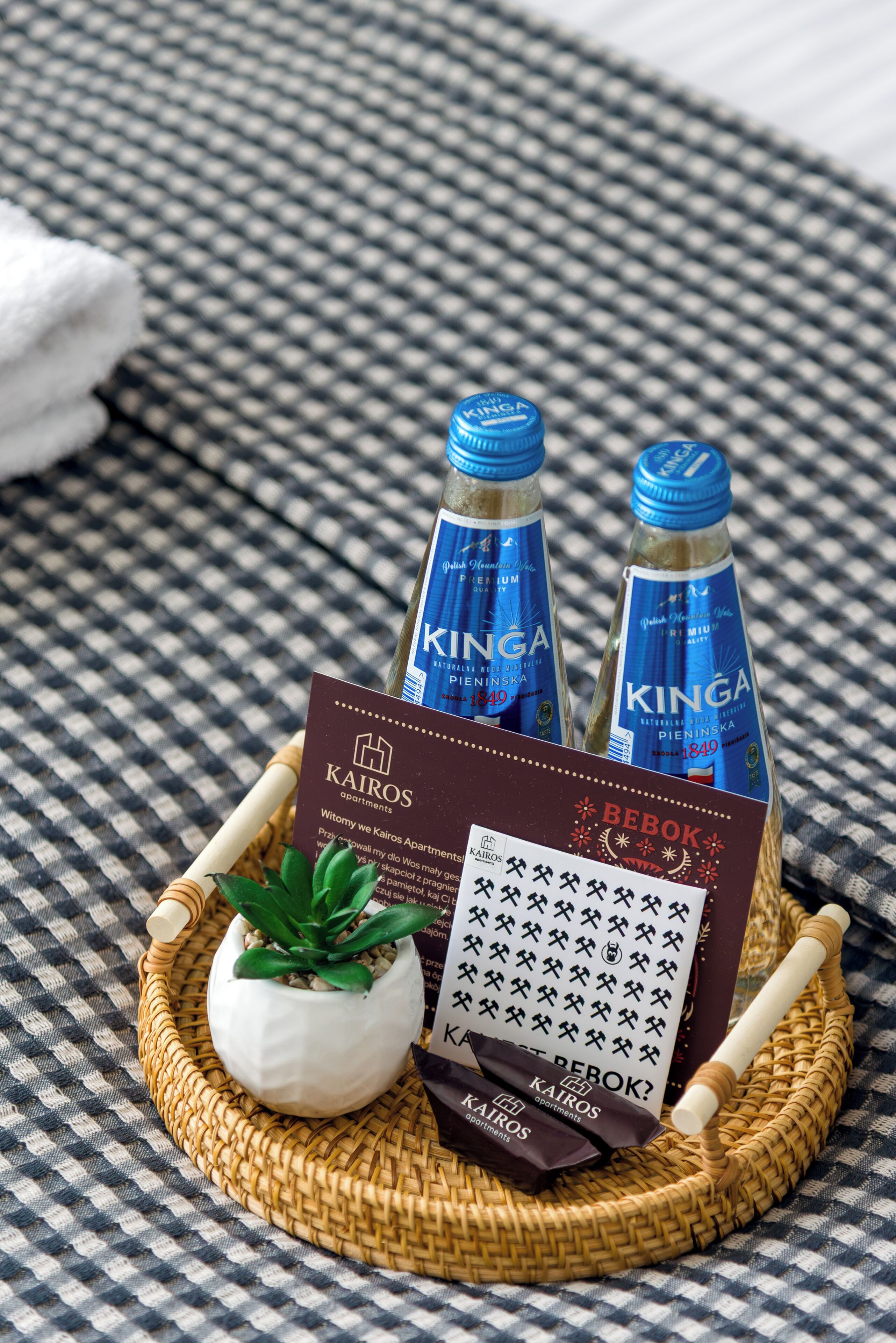 A wicker tray with two bottles of KIngA water, a small potted plant, a card, and a wooden rolling pin.