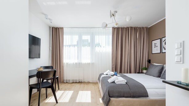 Una habitación de hotel moderna con una cama, un escritorio, una silla, un televisor y una ventana con cortinas.
