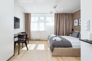 Una habitación de hotel moderna con una cama, un escritorio, una silla, un televisor y una ventana con cortinas.