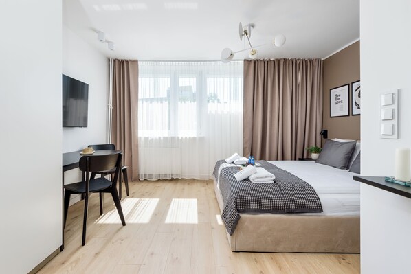 Moderni hotellihuone, jossa on sänky, yöpöytä, tuoli, televisio, verhot ja ikkuna.