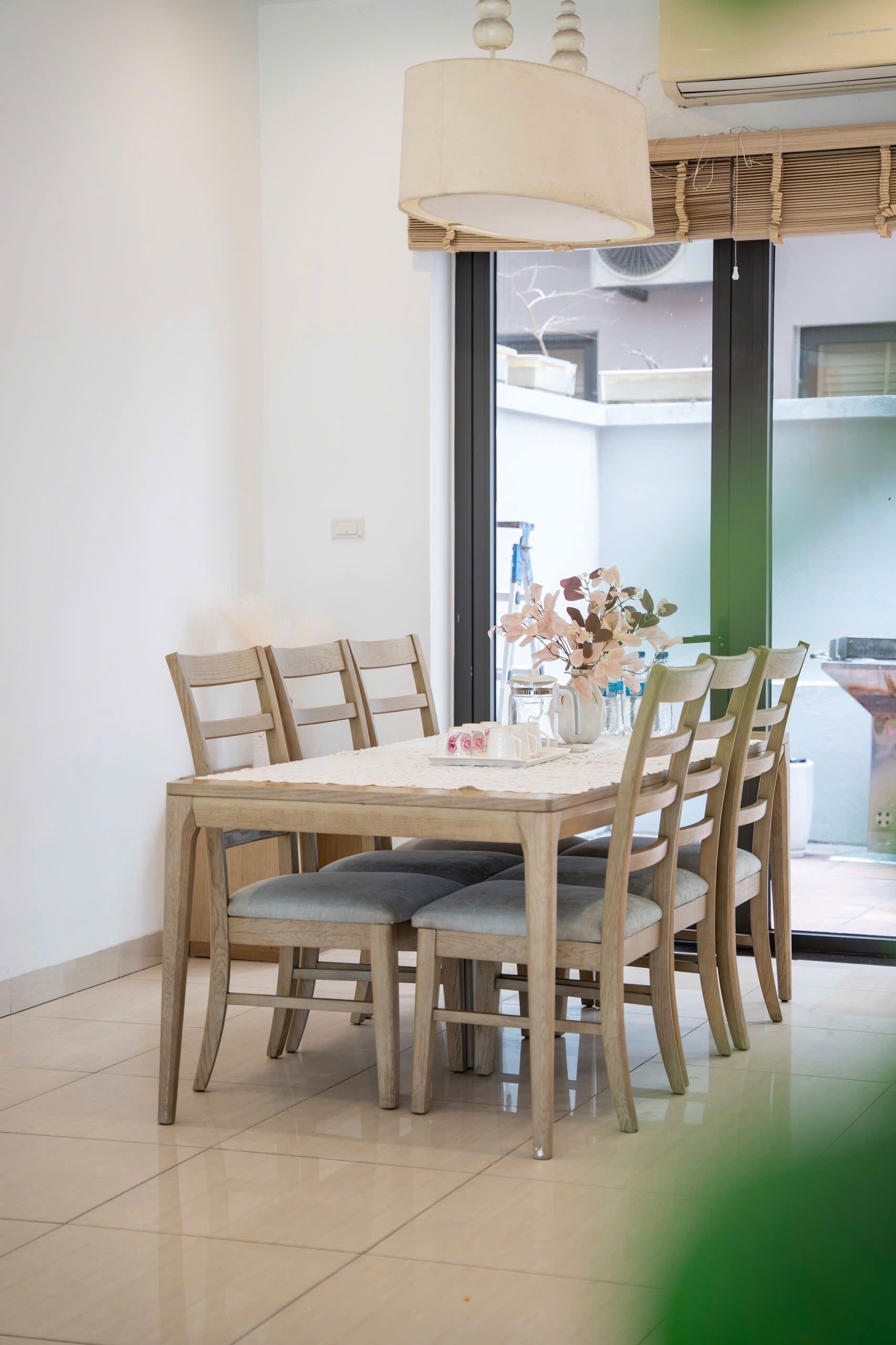 A dining area with a wooden table and chairs, a hanging light fixture, and a view through a glass door.