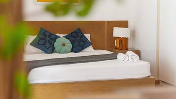 A neatly made bed with patterned pillows, a bedside lamp, and rolled towels.