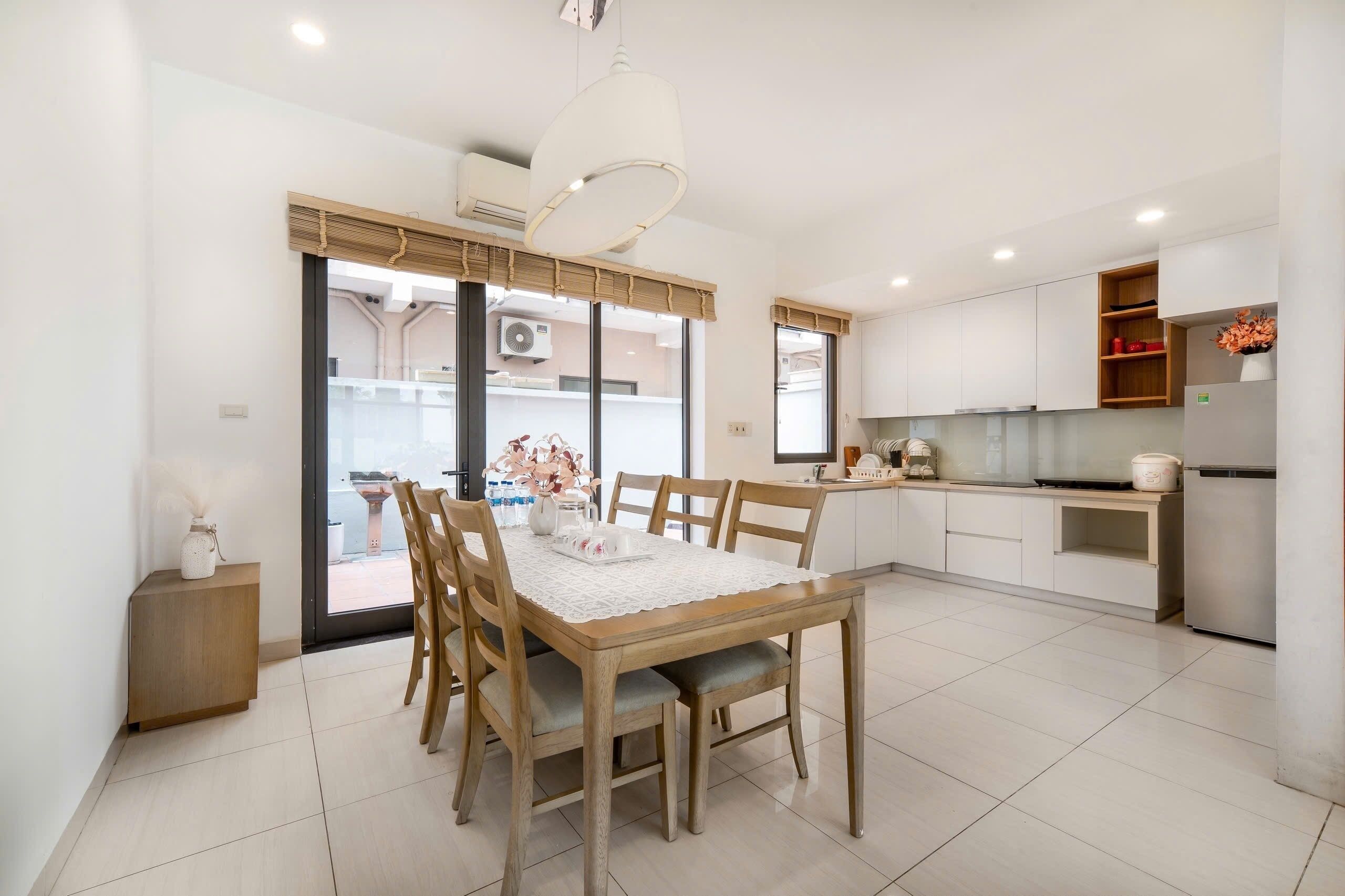 A modern kitchen with white cabinets, a wooden dining table with chairs, and a large window.