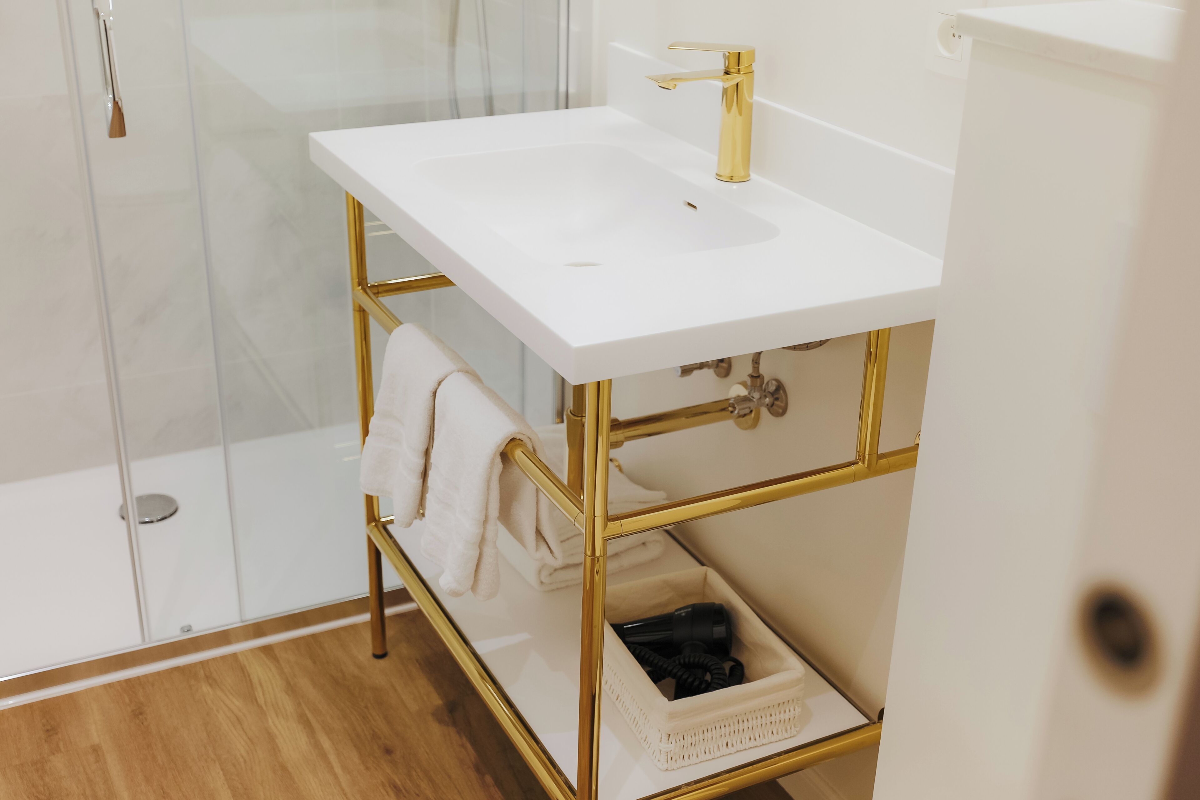 A bathroom with a white sink, gold fixtures, and a glass shower enclosure.