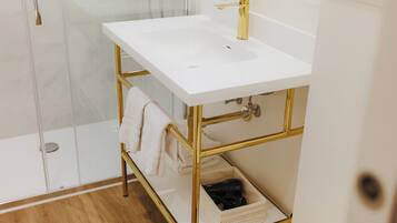 A bathroom with a white sink, gold fixtures, and a glass shower enclosure.