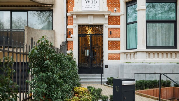 Een gebouw van baksteen met een zwart ijzeren hek en een bord waarop staat: W16 WHITLOCK APARTHOTEL.