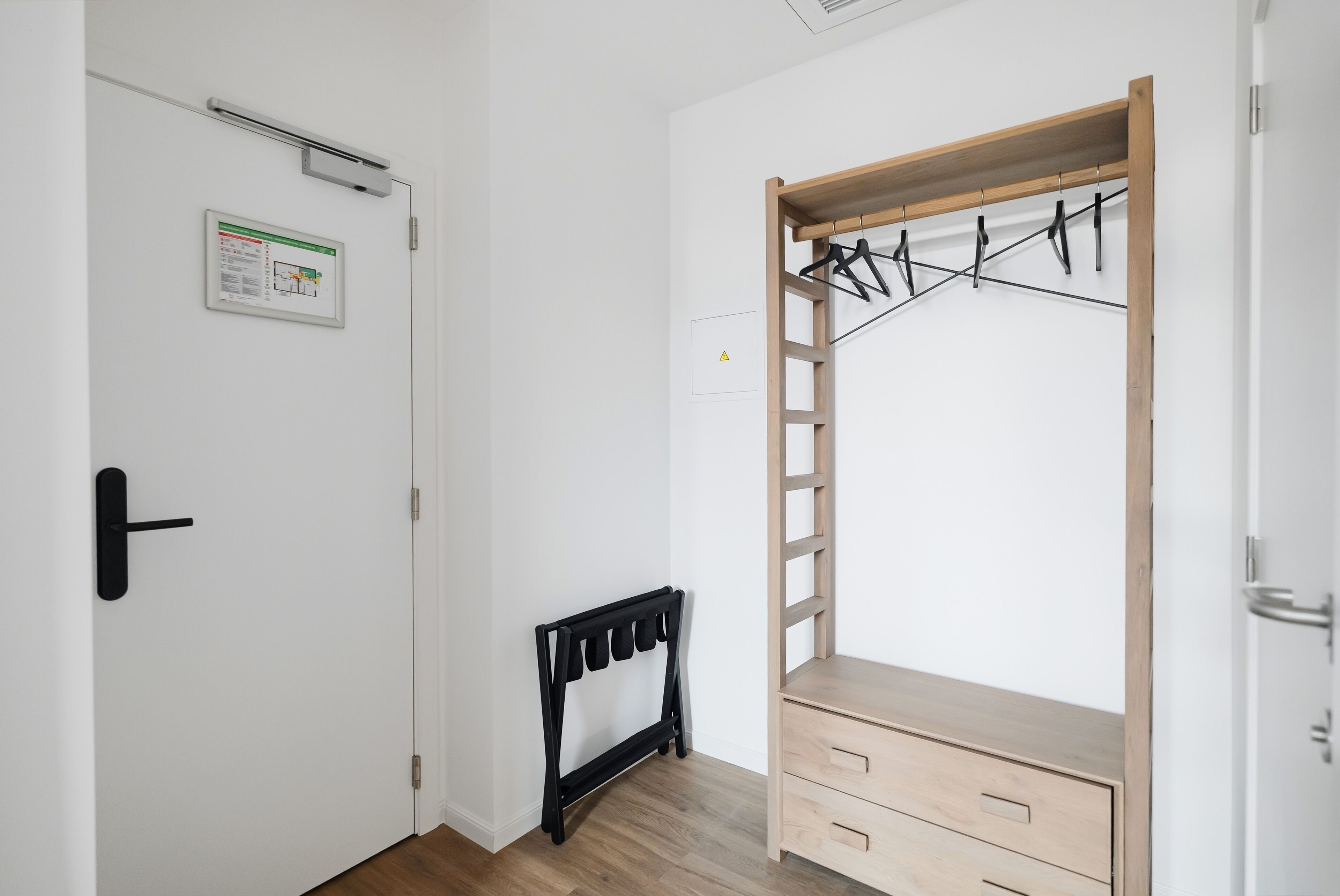 Een kamer met een houten garderobe, een radiator en een deur met een veiligheidssignaal.
